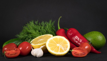 cucumbers, lemon, avocado, red pepper, greens, garlic, tomatoes, on a black background