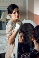Two young women in vintage dresses look at each other through a mirror, a reflection of love. Added a small grain, imitation of film photography