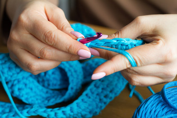 Hands of a young woman knit crochet from blue yarn on a light wooden surface. Start a new bag of yarn.