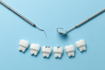 White tooth with caries on blue background  and dentist tools mirror, hook.