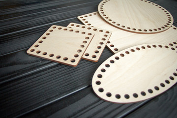 Light wooden parts with holes for making handmade knitted bags on a black surface. Selective soft focus.