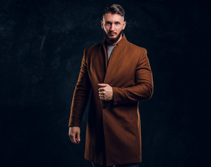 Portrait of a stylish male wearing the demi-season coat. Men's beauty, seasonal fashion. Studio photo against a dark wall background