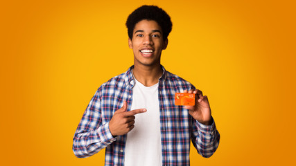 Happy african-american guy holding credit card and point on it
