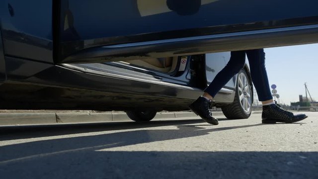 Teen girl in warm clothes gets out of the car and closes the door, feet legs in boots or shoes close-up.