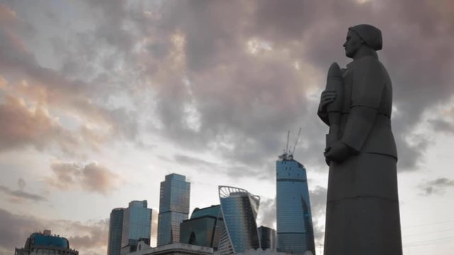 War sculpture of a woman holding a bomb in the new modern buildings background in Moscow city in the evening