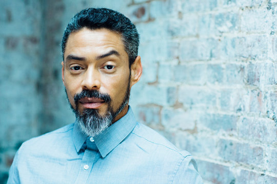  Close Up Portrait Of A Latino Man With Silver Beard And Grey Shirt Looking At Camera