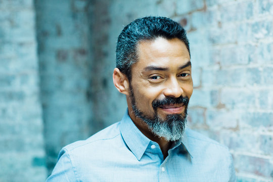 Portrait of a friendly, smiling man with silver beard in grey shirt