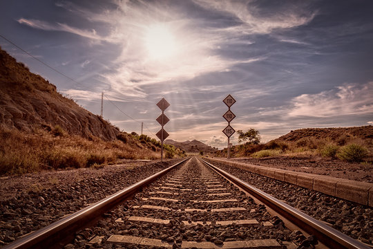 Eine Eisenbahnlinie f&uuml;hrt von der Bildmitte direkt zum Horizont mit der Sonne als Gegenlicht