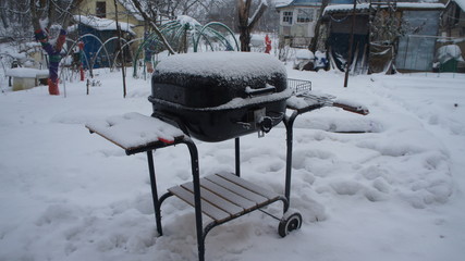 Barbecue grill stands in a rustic courtyard under the snow in winter.