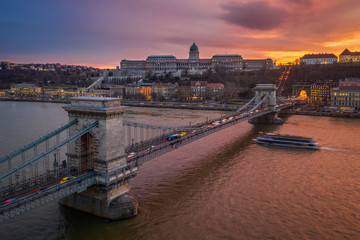 Budapest, Hungary - Aerial view of Szechanyi Chain Bridge and Buda Castle Royal Palace with a beautiful dramatic golden sunset and sightseeing boat on River Danube