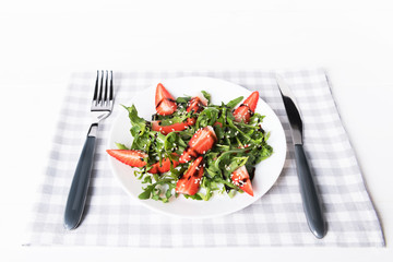 Healthy organic diet salad with arugula, strawberries and sesame in white plate on grey napkin on a white wooden background