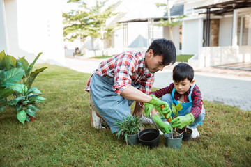 happy asian daddy and son gardening at his house garden together planting new tree