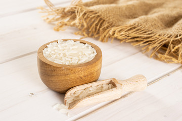 Fototapeta na wymiar Lot of whole white jasmine rice grains in a wooden bowl with wooden scoop on jute cloth on white wood