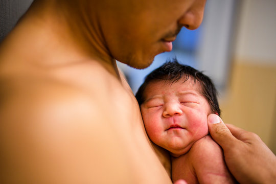 side view of a father holding his newborn baby skin-to-skin
