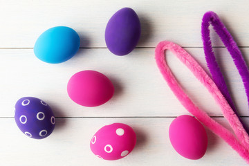 Bunny ears and decorative pink and purple eggs over wooden background