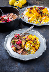 Traditional Iranian khoresh beh stew with chunks of lamb, quinces and saffron rice as closeup in a cast-iron roasting dish and pewter plate