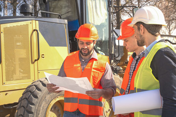 male workers engineers in helmets are watching the drawings near the bulldozer and excavator