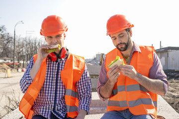 two workers in helmets lunch, rest, sit on concrete slabs