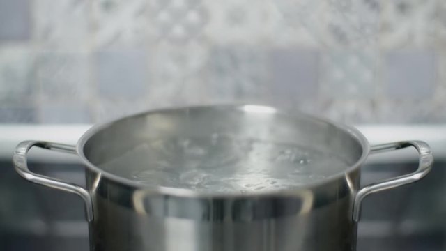 Water boils in metal pan on kitchen in living apartment, induction electric hotplate, boiling in slow motion, food cooking