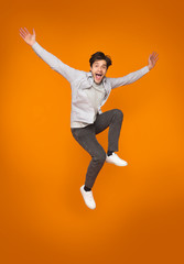 Fototapeta na wymiar Funny man jumping with raised arms over orange background