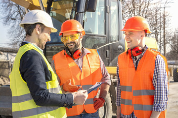 male workers engineers in helmets talking near the bulldozer and excavator