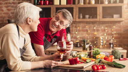 Senior couple enjoying wine during lunch preparing in kitchen,