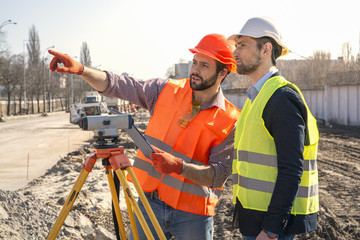 two male surveyor engineer with a device working on a construction site in a helmet - obrazy, fototapety, plakaty