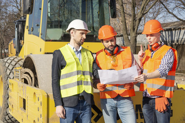 male workers engineers in helmets are watching the drawings near the bulldozer and excavator © Vasiliy