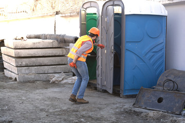 worker engineer in helmet at a construction site runs to the restroom