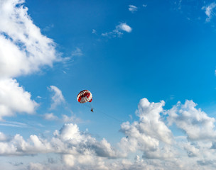 Silhouette of people on a parachute flying behind a motorboat on a holiday by the sea against the blue sky with clouds