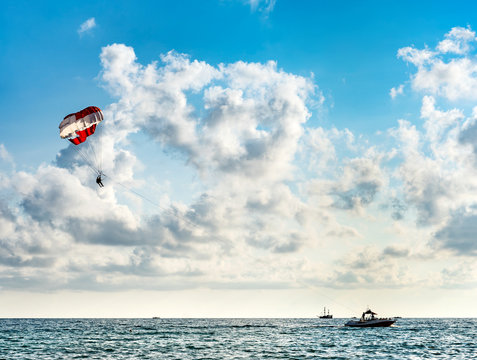 Silhouette of people on a parachute flying behind a motorboat on a holiday by the sea against the blue sky with clouds