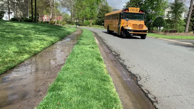Yellow public school bus driving through a neighborhood on a spring afternoon