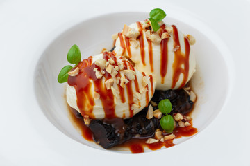 vanilla ice cream balls with caramel sauce, dried prunes and microgreens on white plate. Close-up