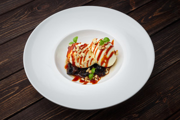 vanilla ice cream balls with caramel sauce, dried prunes and microgreens. Brown wooden background