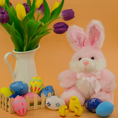 Easter decoration with rabbit, eggs and tulips on orange background. 