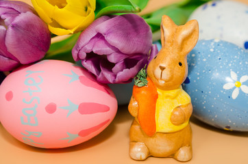 Easter decoration with rabbit, eggs and tulips on orange background. 