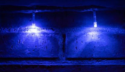 A brick wall is illuminated only by two small blue lights. These lights generate an interplay of lights and shadows on the wall. Horizontal photo
