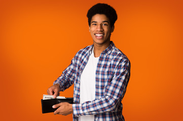 Money saving. African-american guy putting banknotes into wallet