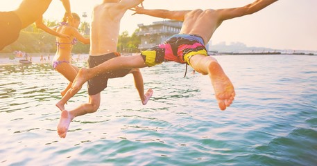 Group of happy crazy people having fun jumping in the sea water from boat. Friends jump in mid air...