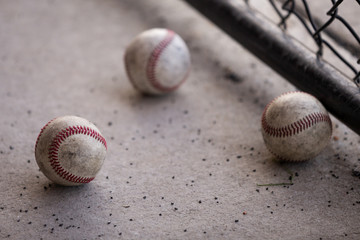 Close-up of three baseballs on the concrete ground of the dugout next to a chainlink fence