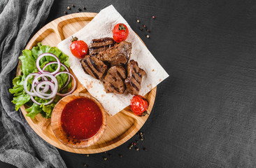 Grilled beef meat and vegetables with fresh salad and bbq sauce on cutting board over black stone background. Hot Meat Dishes. Top view, flat lay, copy space
