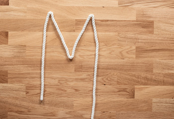 The letter M formed with white rope on a wooden table