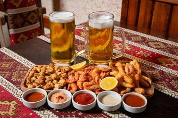 Beer set.Two Beers and appetizers on a wooden plate with five sauces.On a wooden table with a tablecloth with national patterns.