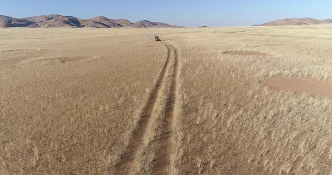 4K front aerial view of a 4x4 safari vehicle driving on a sand track through the African savannah grasslands with the famous fairy circles, Namibia