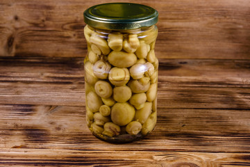 Glass jar with canned mushrooms on wooden table