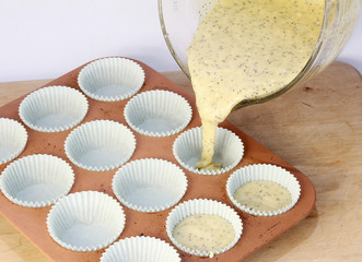 Batter for Lemon Poppy Seed cupcakes being poured from mixing bowl into muffin pan.
