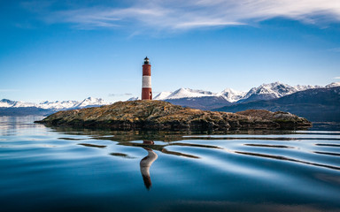 The lighthouse at world's end. Island with lighthouse on a peaceful lake, snowy mountains landscape on a perfect weather day. - obrazy, fototapety, plakaty