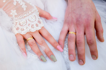 Hands with wedding rings on the nameless finger on the background of a wedding dress.