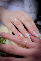 Hands with wedding rings on the background of a bouquet with white roses.