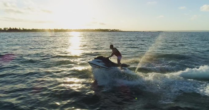 4K aerial close-up view of man having fun riding a Jet Ski in the ocean with the sun setting on the waves, Mozambique